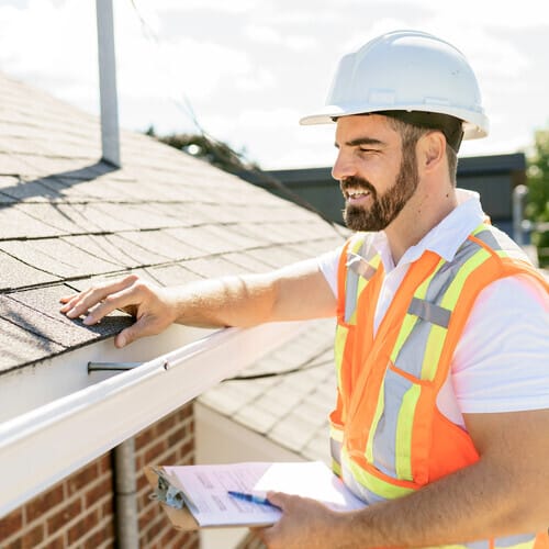 A man in a hard hat, holding a clipboard, standing on the steps of a house